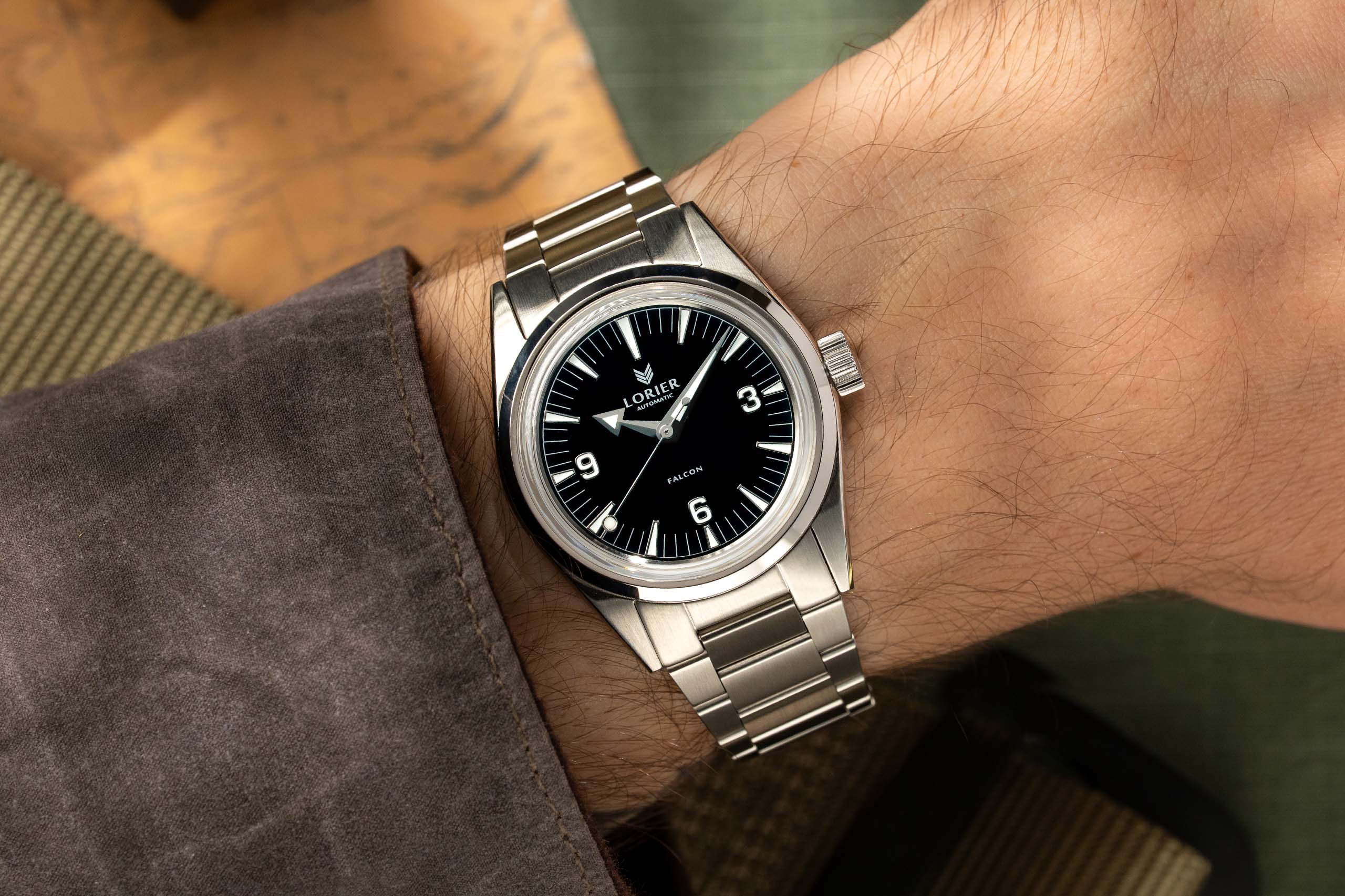 A wrist wearing a stainless steel Lorier Falcon watch with a black dial, shown in a close-up lifestyle shot.