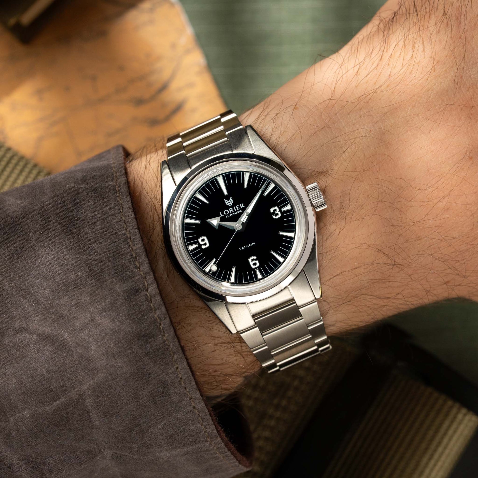 A wrist wearing a stainless steel Lorier Falcon watch with a black dial, shown in a close-up lifestyle shot.