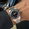 A Lorier Hyperion watch with a stainless steel bracelet and a distinctive red and blue bezel, shown worn on a wrist.