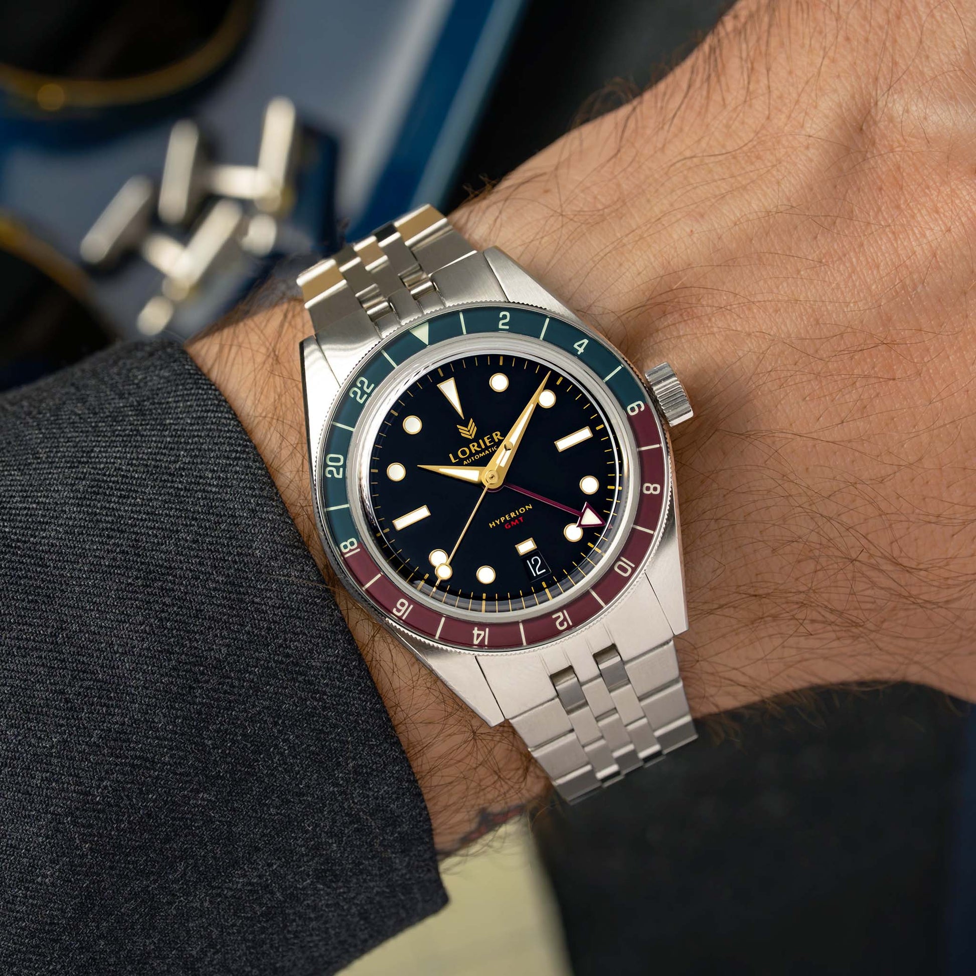 A Lorier Hyperion watch with a stainless steel bracelet and a distinctive red and blue bezel, shown worn on a wrist.