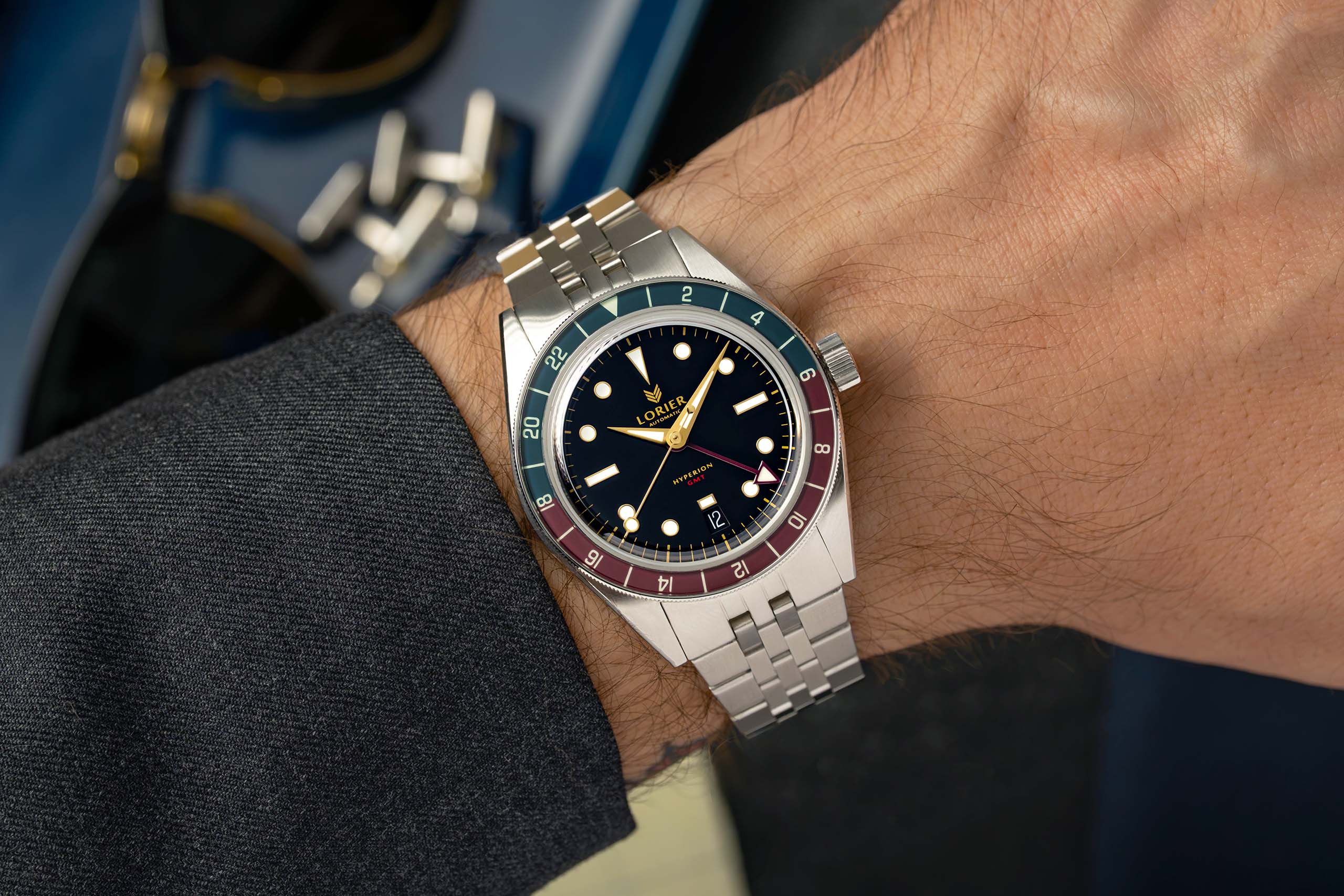 A Lorier Hyperion watch with a stainless steel bracelet and a distinctive red and blue bezel, shown worn on a wrist.