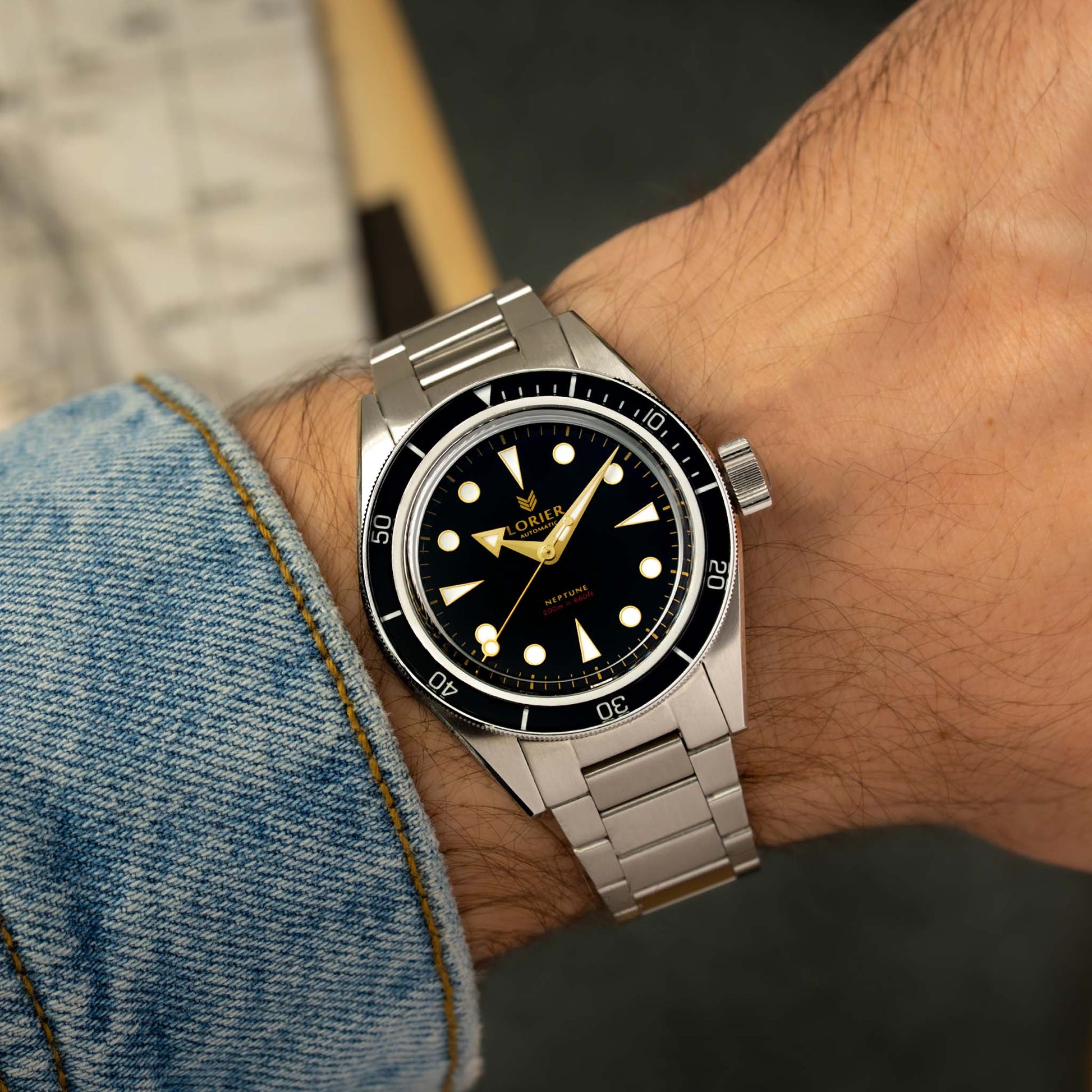 A Lorier Neptune watch with a black dial and stainless steel bracelet, shown worn on a person's wrist with a denim sleeve visible.