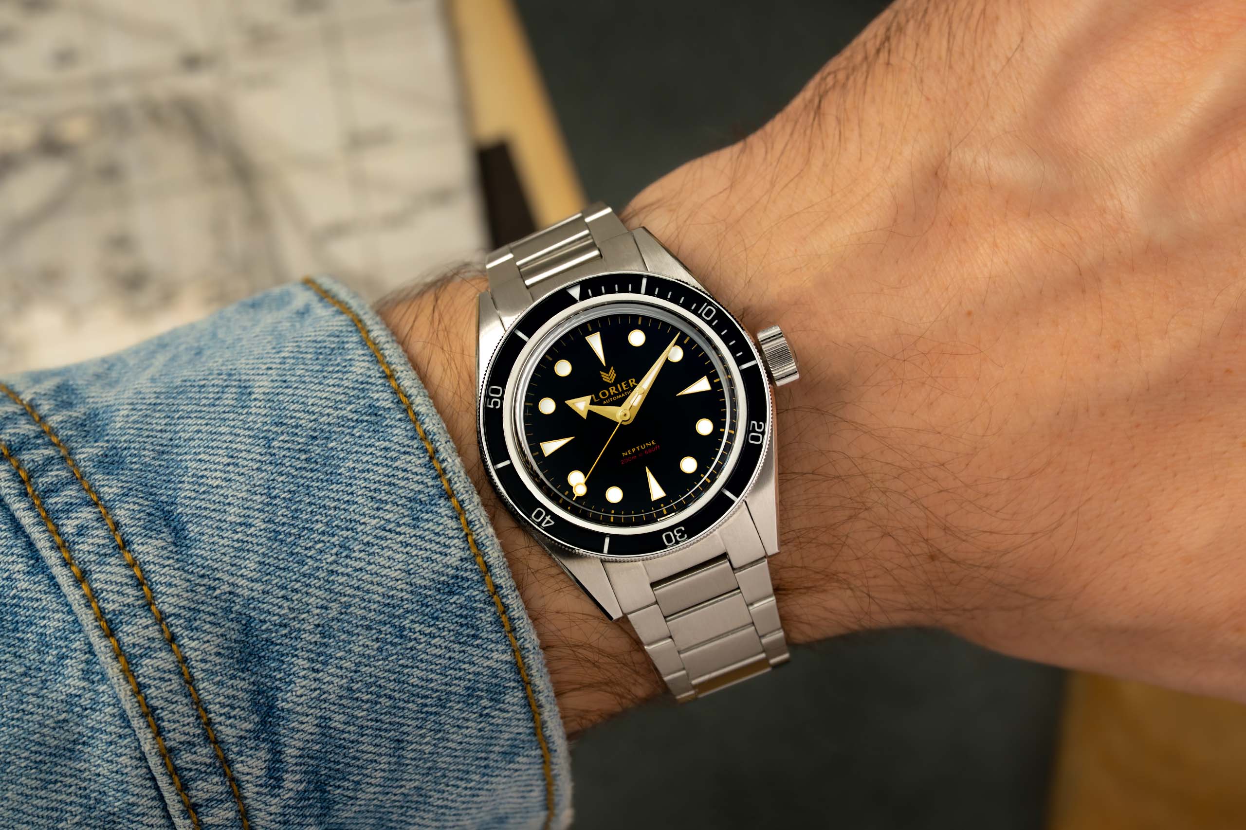 A Lorier Neptune watch with a black dial and stainless steel bracelet, shown worn on a person's wrist with a denim sleeve visible.